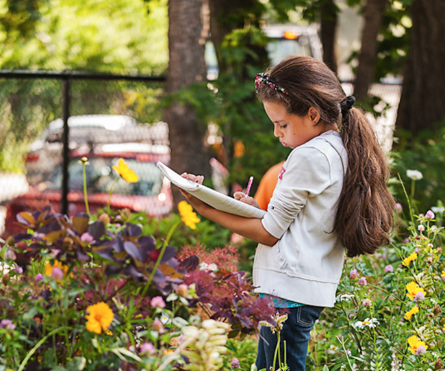 Young female student surveying garden and writing down observations on notebook